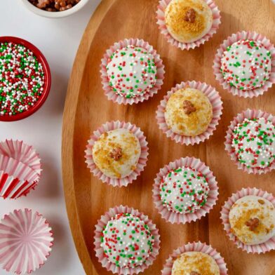 A wood plate containing gingerbread cookie balls and small bowls of sprinkles