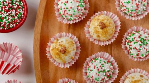 A wood plate containing gingerbread cookie balls and small bowls of sprinkles