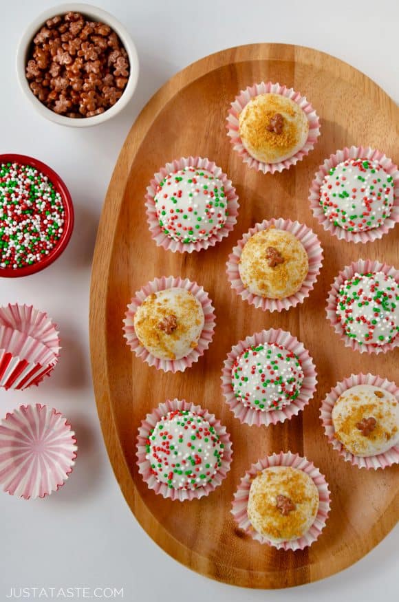 A wood plate containing gingerbread cookie balls and small bowls of sprinkles