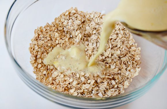 Wet ingredients being poured into glass bowl containing dry ingredients for oatmeal cups