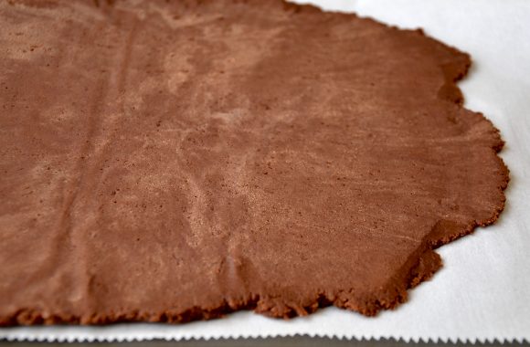 Chocolate sugar cookie dough rolled out on white parchment paper