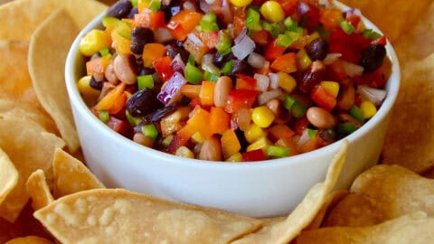 A white bowl with Texas Caviar on a plate containing tortilla chips.