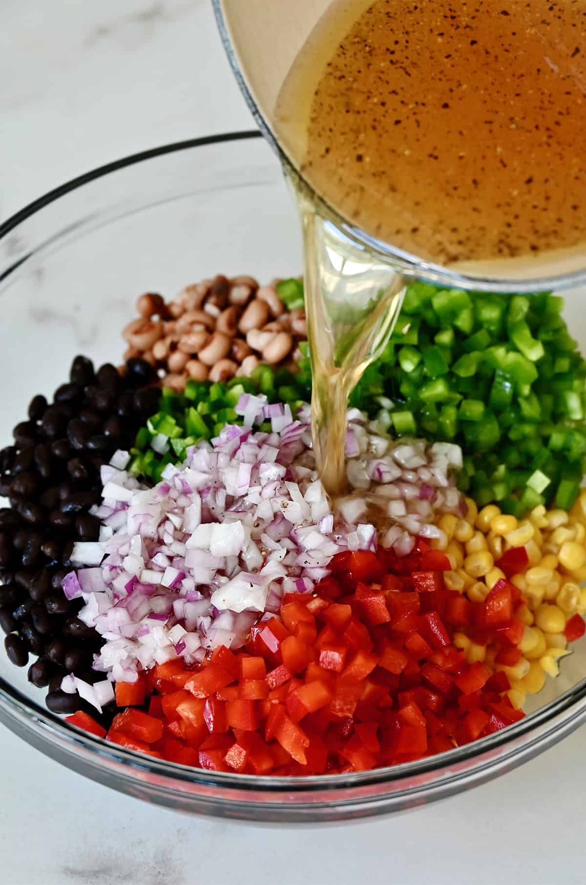 Apple cider vinegar and oil dressing being poured over cowboy salad in a bowl.