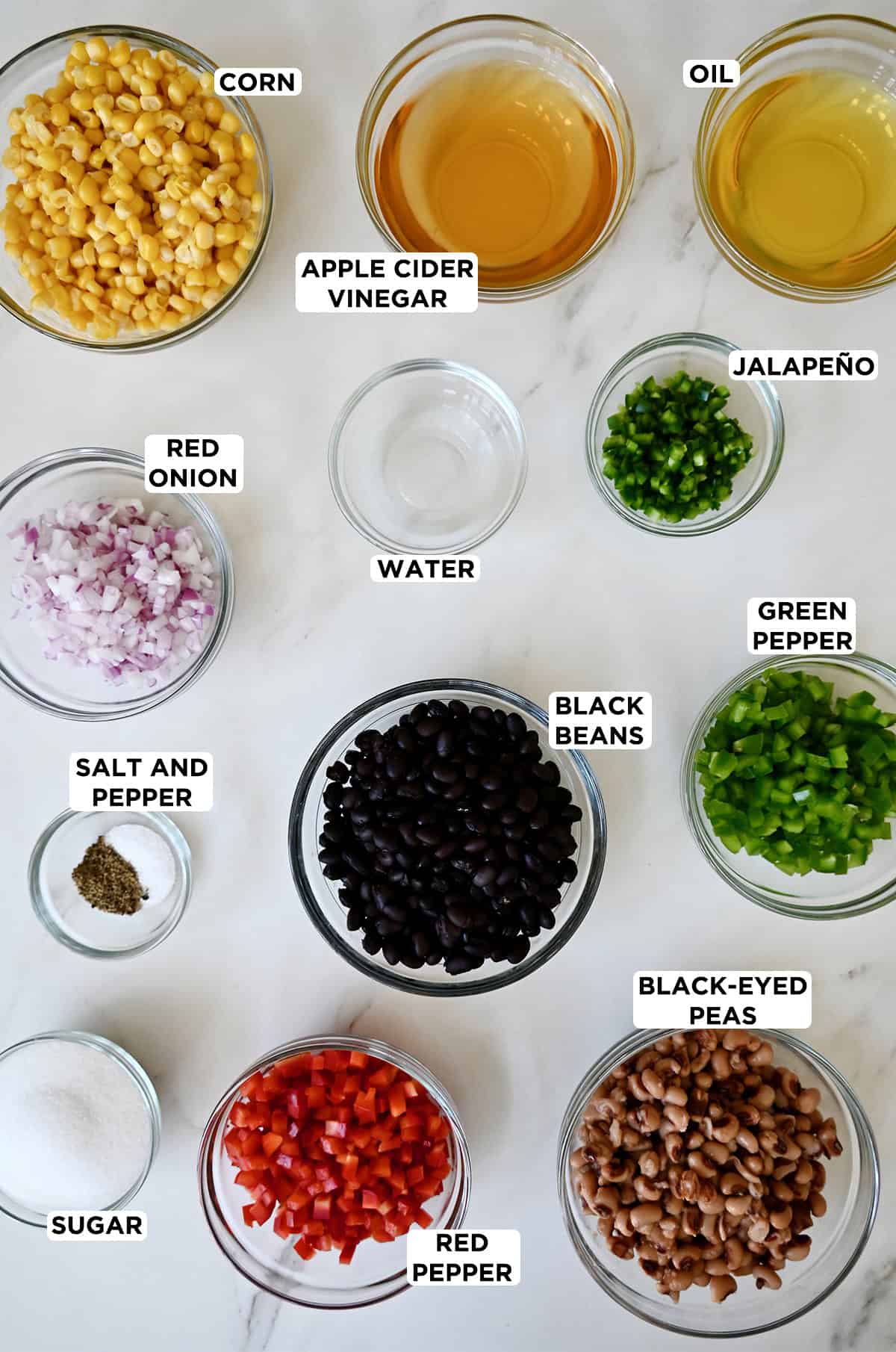 Cowboy caviar ingredients in various sizes of glass bowls, including corn kernels, apple cider vinegar, oil, diced jalapeño, chopped red and green bell peppers, black beans, black-eyed peas, sugar, salt and pepper, and diced red onion. 