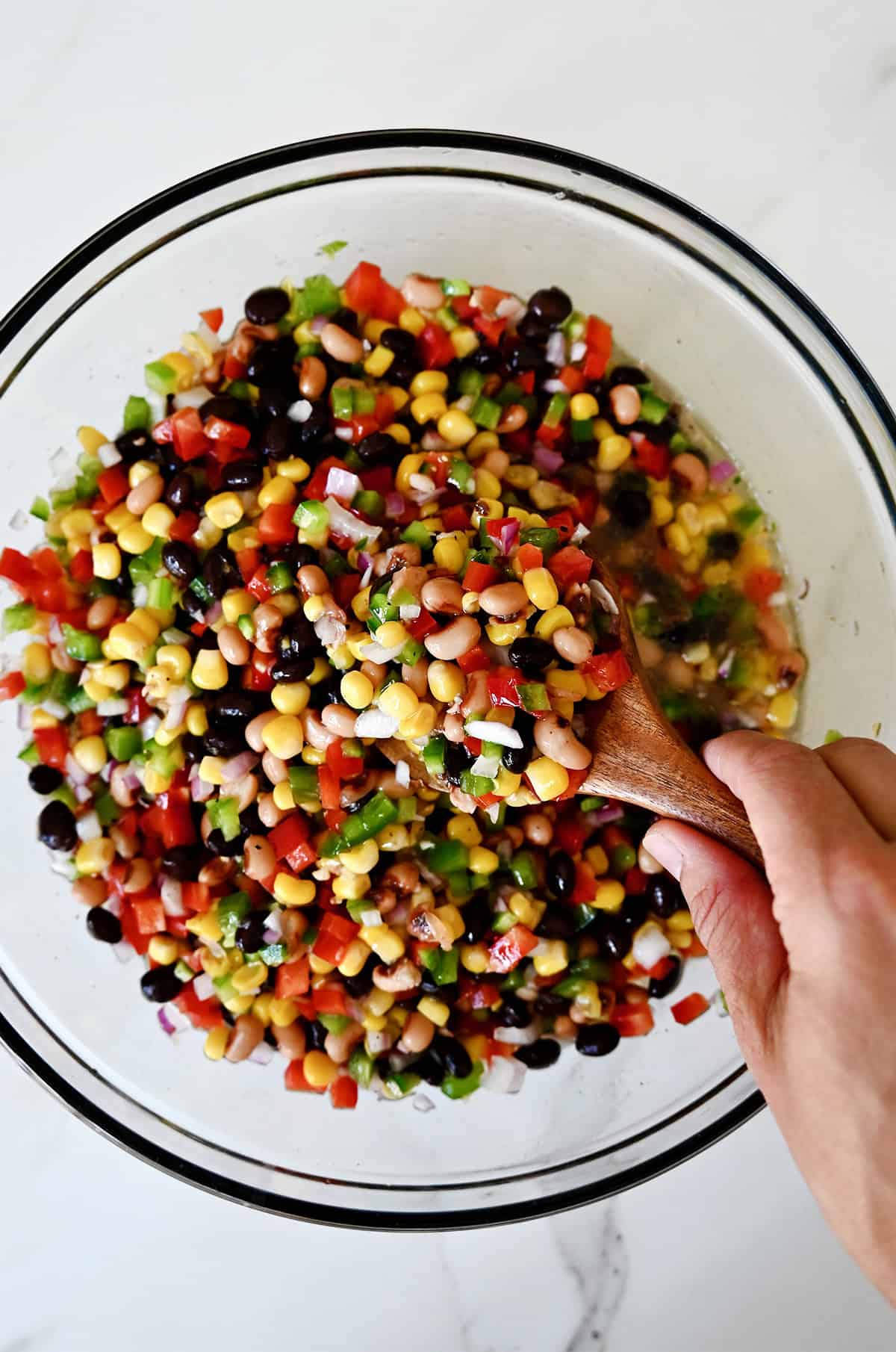 A hand holding a spoon mixes together Texas caviar with its dressing.