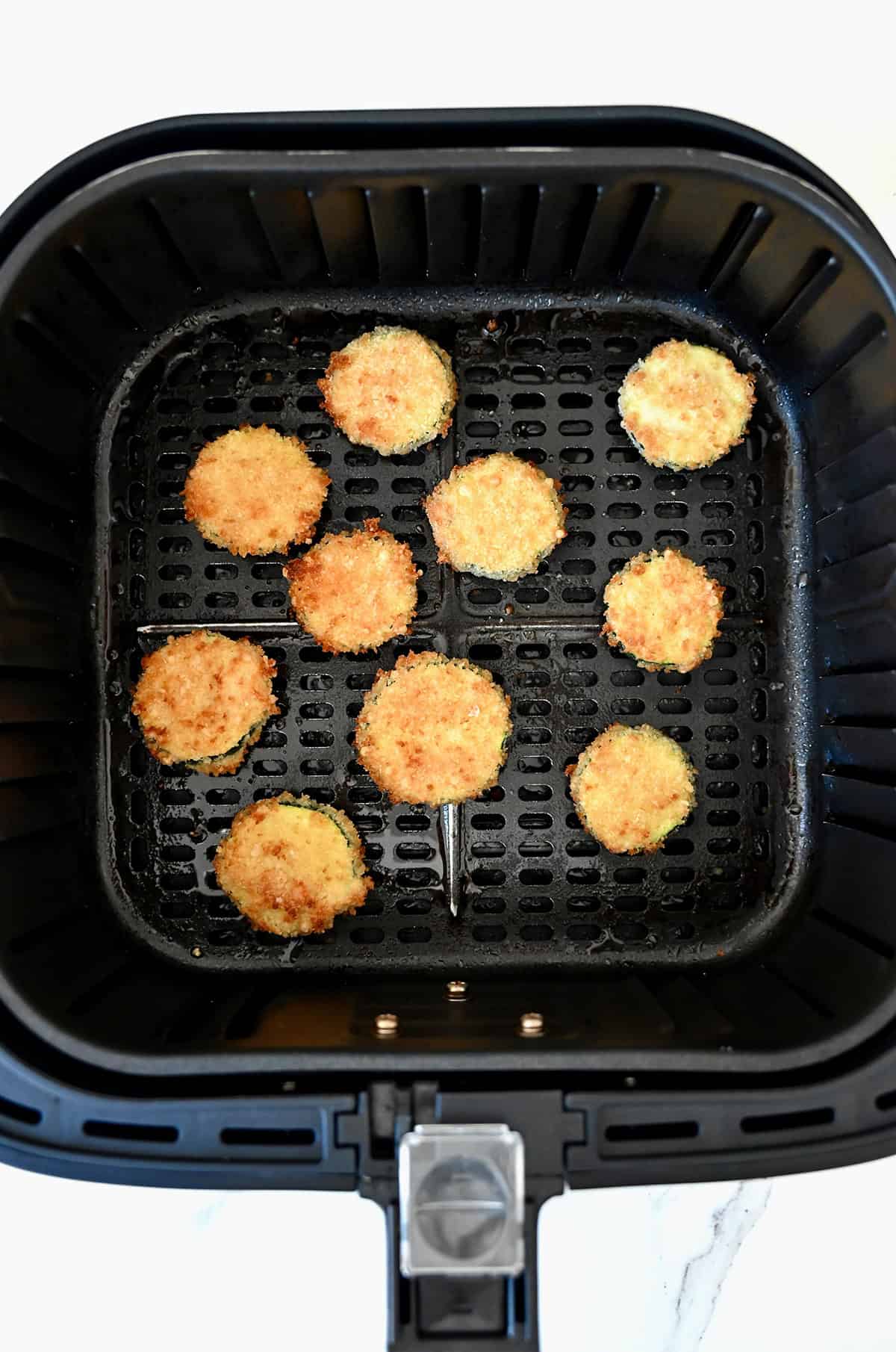 Golden brown, crispy air fryer zucchini chips in the basket of an air fryer.