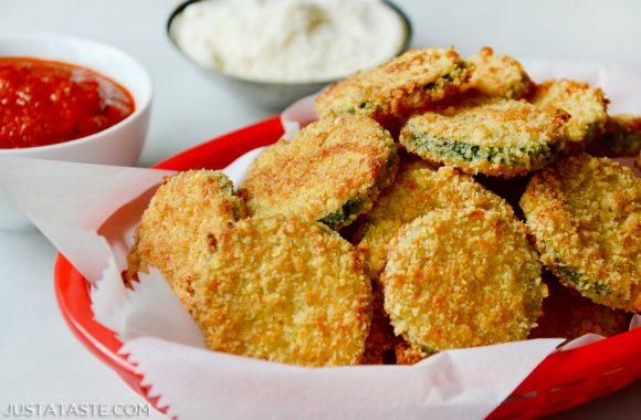 Baked Parmesan Zucchini Chips in white food paper lined red basket with ketchup and mayonnaise in background.