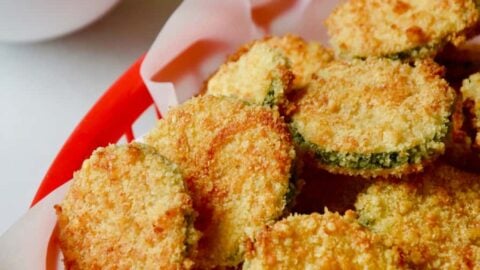 Baked Parmesan Zucchini Chips in red basket lined with white food paper with ketchup and mayonnaise in the background.