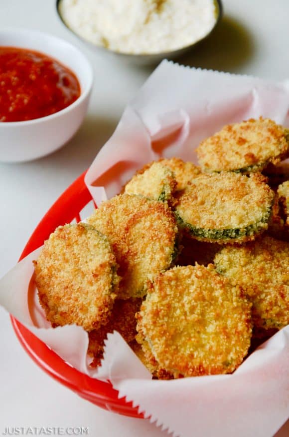 Baked Parmesan Zucchini Chips in red basket lined with white food paper with ketchup and mayonnaise in the background.