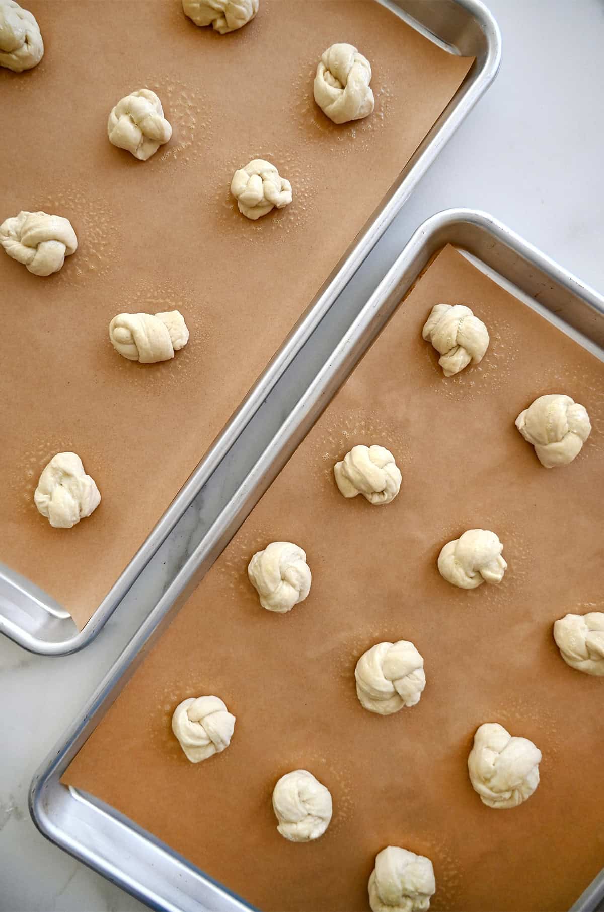 Unbaked knots from pizza dough on two baking sheets lined with parchment paper.