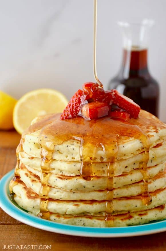 Lemon Poppyseed Pancakes topped with strawberries and maple syrup on blue plate with half a lemon and maple syrup in background.