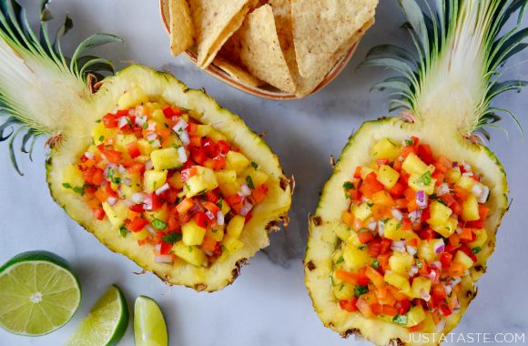 Two pineapple boats filled with The Best Pineapple Salsa next to a cut lime and small bowl of tortilla chips.