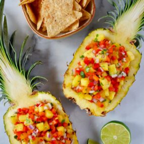 Two pineapple boats filled with The Best Pineapple Salsa with a cut lime and small bowl of tortilla chips.