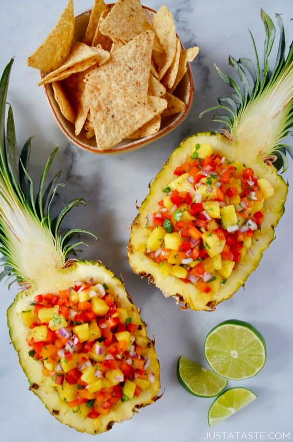 Two pineapple boats filled with The Best Pineapple Salsa with a cut lime and small bowl of tortilla chips. 