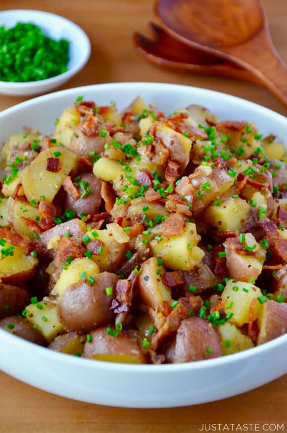 White bowl with Potato Salad with Warm Bacon Dressing next to small white bowl filled with fresh chives and wooden serving spoon and fork.