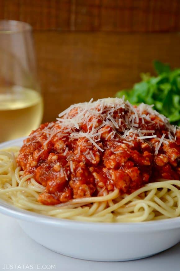 Quick Spaghetti Bolognese with Turkey garnished with shredded Parmesan cheese in white bowl with glass of white wine in background