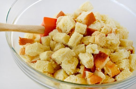 A glass bowl containing diced brioche bread and an orange spatula