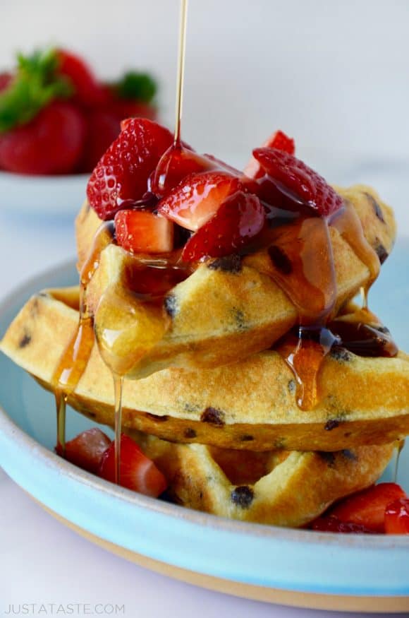 Stack of Buttermilk Chocolate Chip Waffles topped with strawberries and maple syrup on pale blue plate.