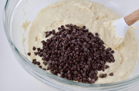 Waffle batter with mini chocolate chips in glass bowl with spatula.