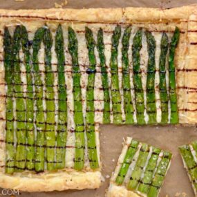 Cheesy Asparagus Tart drizzled with balsamic syrup with corner cut into two pieces on brown paper.