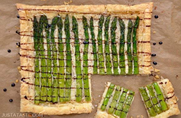 Cheesy Asparagus Tart drizzled with balsamic syrup with corner cut into two pieces on brown paper.