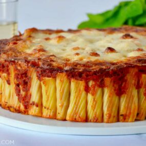 Easy Cheesy Rigatoni Pie on white serving plate with basil and two glasses in the background