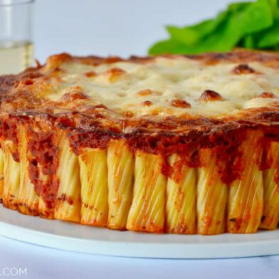 Easy Cheesy Rigatoni Pie on white serving plate with basil and two glasses in the background