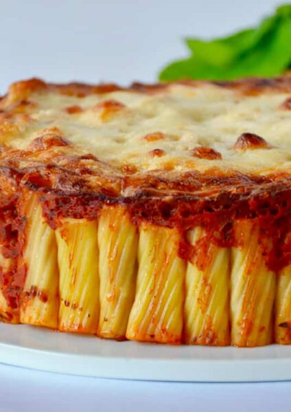 Easy Cheesy Rigatoni Pie on white serving plate with basil and two glasses in the background
