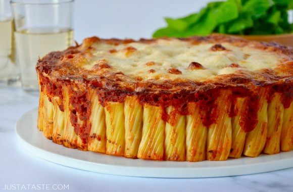 Easy Cheesy Rigatoni Pie on white serving plate with basil and two glasses in the background