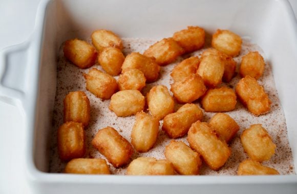 Easy Churro Bites in white bowl with cinnamon-sugar mixture.