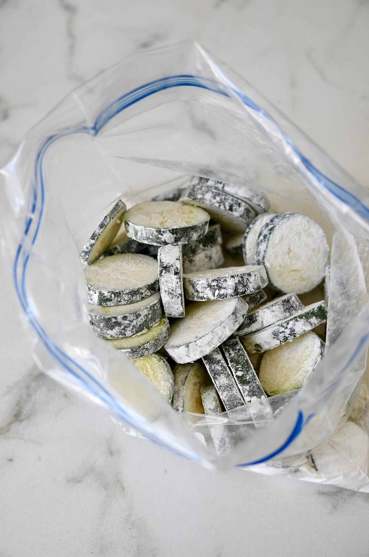Slices of zucchini coated in flour in a plastic ziplock bag.