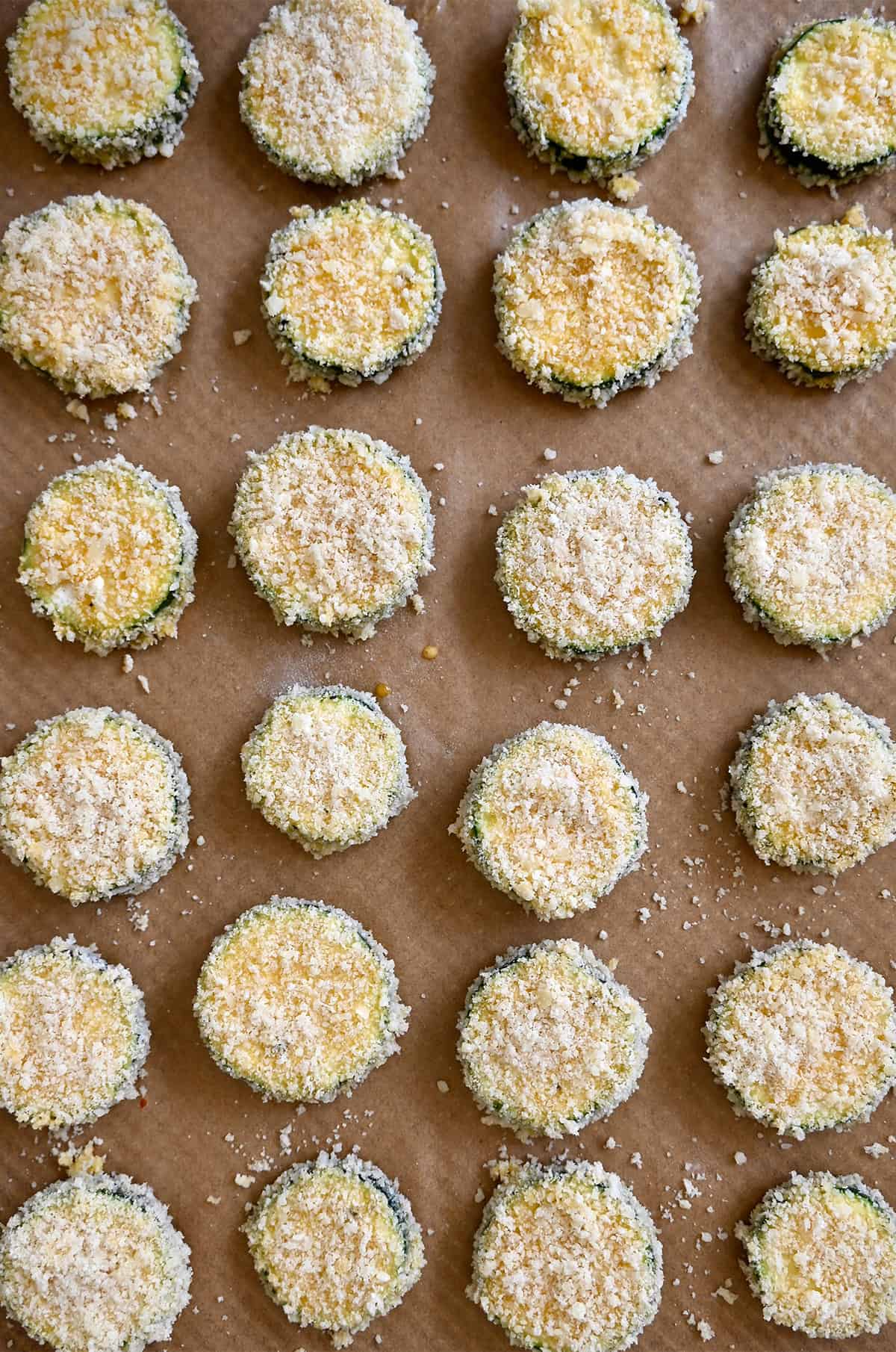 Breaded zucchini chips with parmesan on a parchment paper-lined baking sheet.
