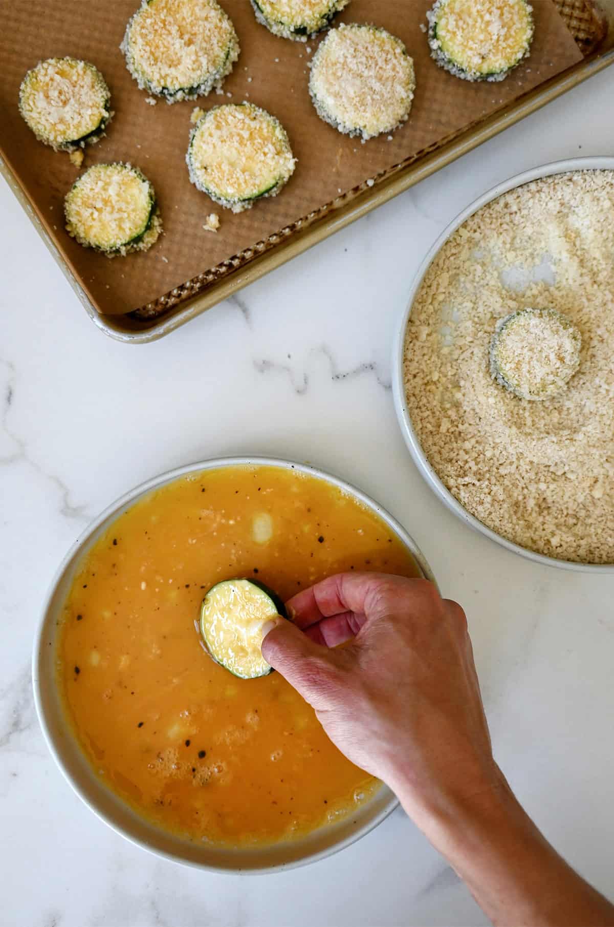 Breading station for dredging zucchini chips, which includes a shallow bowl containing whisked eggs and another shallow bowl with Panko breadcrumbs.