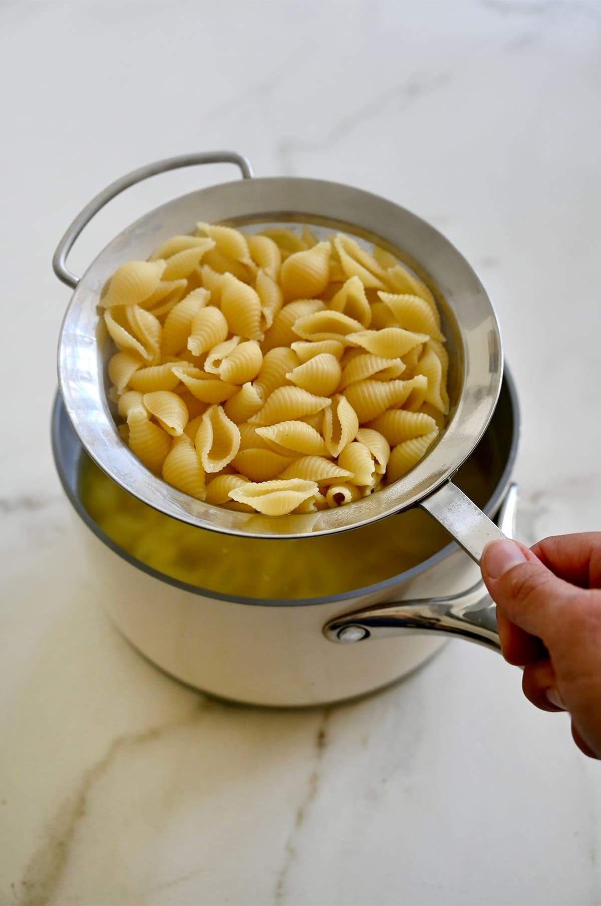 Cooked macaroni pasta in a mesh strainer over a pot.