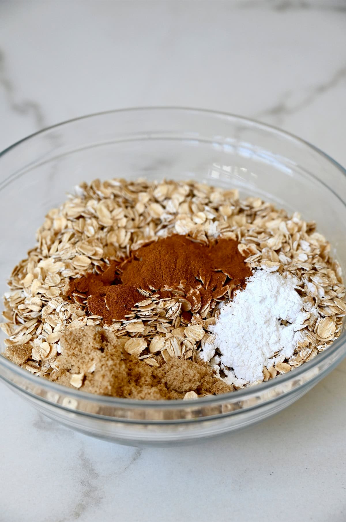 Rolled oats, cinnamon, brown sugar and baking powder in a glass bowl.