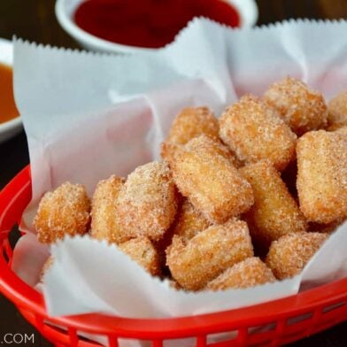 Easy Churro Bites in red basket lined with white food paper with dipping sauces in background.