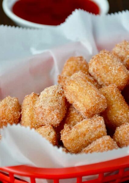 Easy Churro Bites in red basket lined with white food paper with dipping sauces in background.