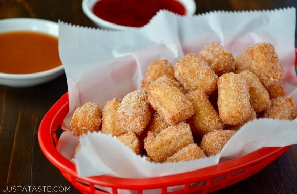 Easy Churro Bites in red basket lined with white food paper with dipping sauces in background.