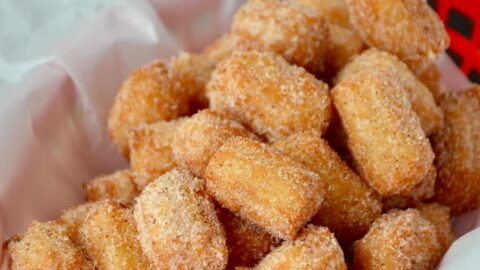 Easy Churro Bites in red basket lined with white food paper with dipping sauces in background.