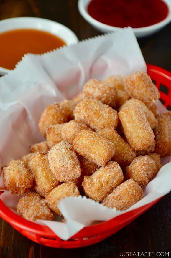 Easy Churro Bites in red basket lined with white food paper with dipping sauces in background.