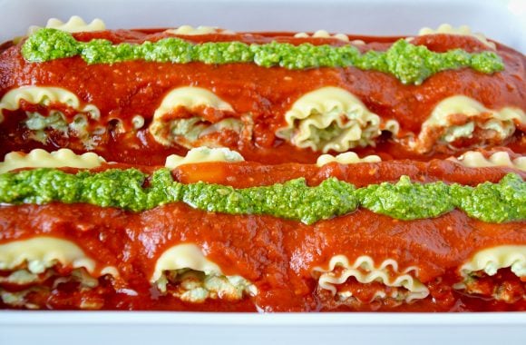 Easy Lasagna Roll-ups topped with marinara and pesto in white baking dish