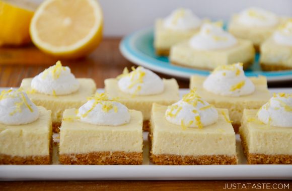 Square-cut Easy Lemon Cheesecake Bars on white plate with cut lemon and more bars on a blue plate in background.