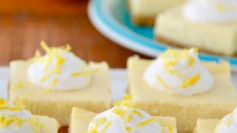 Easy Lemon Cheesecake Bars on white plate with cut lemon and more bars on a blue plate in background.