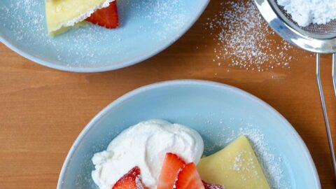 Two pale blue plates with Strawberry Cream Cheese Crêpes topped with fresh strawberries, whipped cream and powdered sugar.