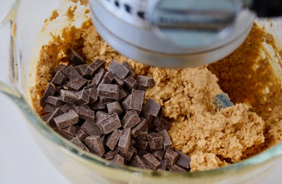 Flourless chocolate chip oatmeal cookie dough with chocolate chunks in a glass stand mixer bowl with beater attachment.