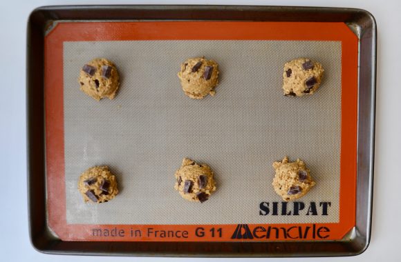 Six balls of flourless oatmeal chocolate chip cookie dough on silpat lined baking sheet.