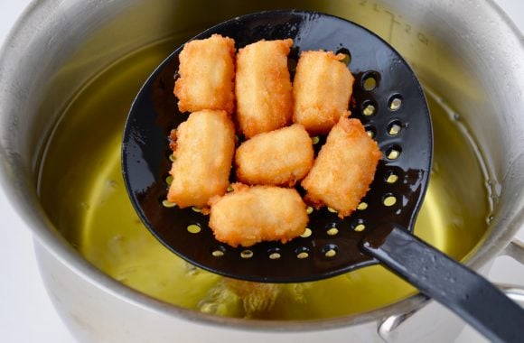 Stockpot with hot oil and slotted spoon with fried churro bites.