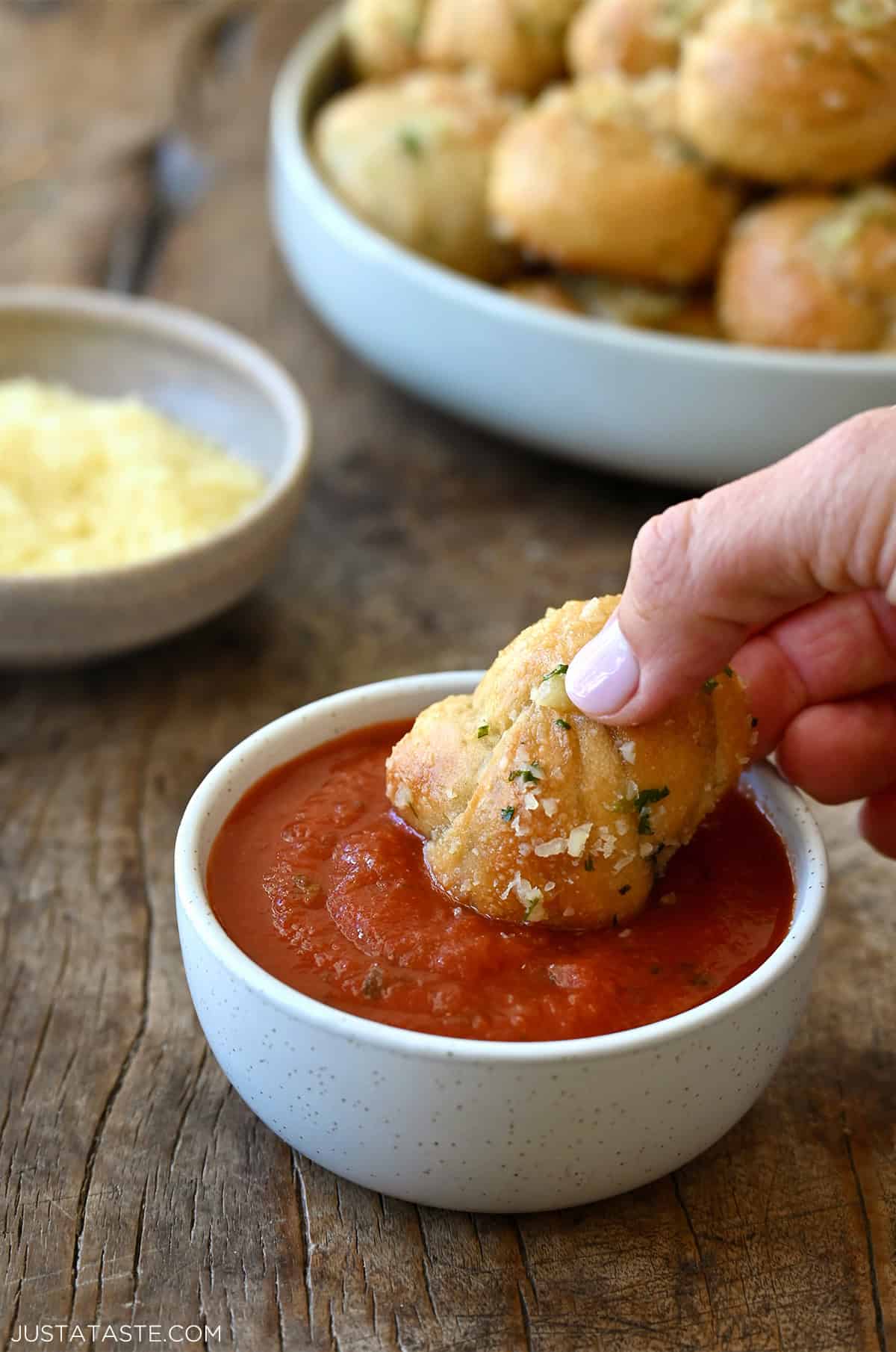 Dipping a garlic knot into warm marinara sauce in a small bowl.