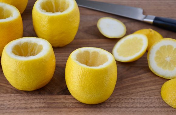 A wood cutting board containing hollowed out lemons and a knife