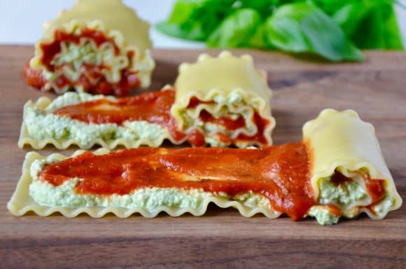 Lasagna Roll-ups being rolled on wooden cutting board with basil in background